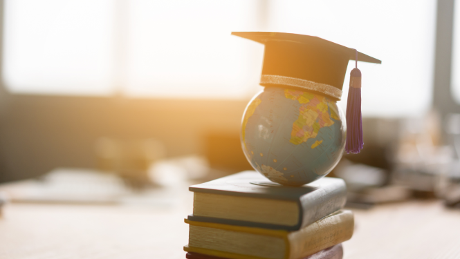 stāv grāmatu kaudzīte, uz tās globuss ar absolventa cepuri