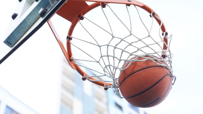 Basketbola bumba iekrīt grozā, fonā gaišas debesis