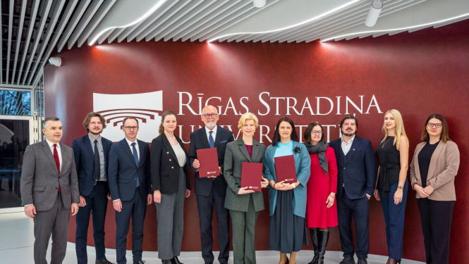 RSU un IZM pārstāvju kopbilde pie sienas, kur redzams Rīgas Stradiņu universitātes logo.