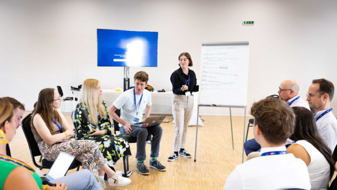 Cilvēki sēž aplītī un apspriežas. 