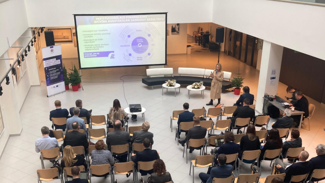 Konference, cilvēki sēž zālē, Diāna Laipniece prezentē