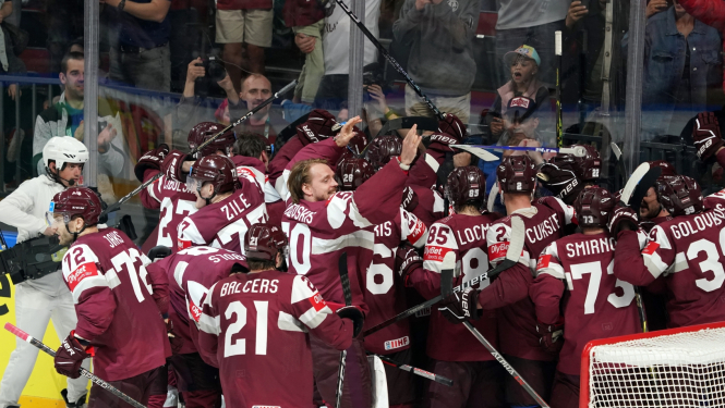 Latvijas hokeja izlase sarkanajos formas tērpos. Komandas biedri apskaujas visi kopā pēc uzvaras.