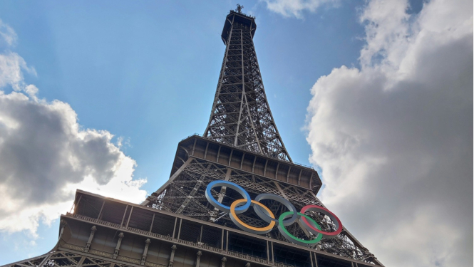 Eifeļa tornis ar olimpiskajiem riņķiem uz mākoņu fona