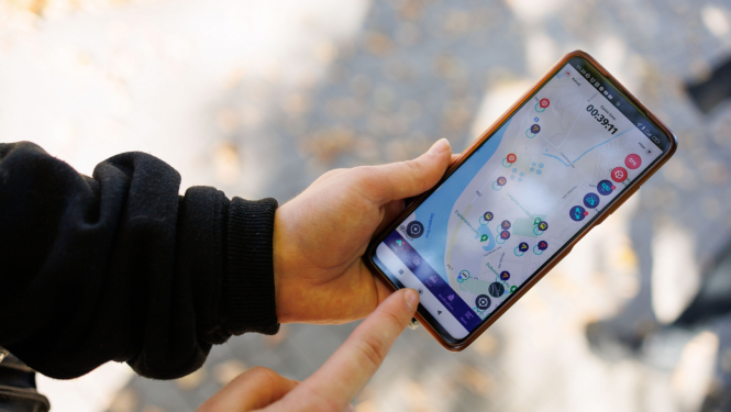 Jaunieša rokas tur rokās telefonu, kura ekrānā ir karte ar atzīmētiem apskates objektiem