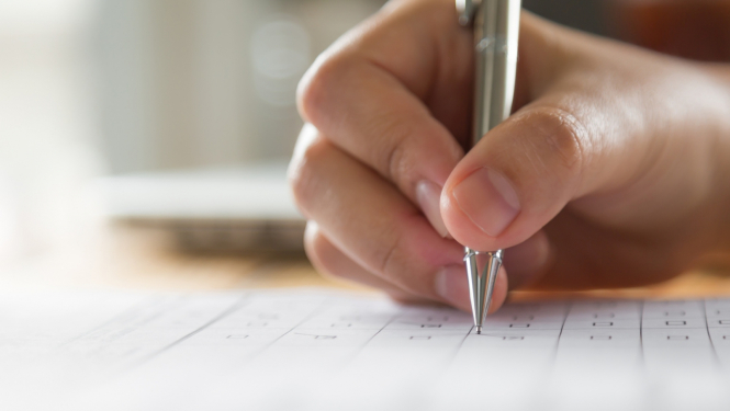 Cilvēka roka tur pilspalvu un atzīmē izvēlēto atbildes variantu lapā