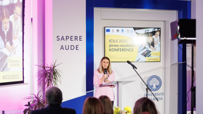 Inita Juhņēviča saka uzrunu konferencē, aizmugurē liels ekrāns ar uzrakstu "ICILS 2023 pirmo rezultātu prezentācija"