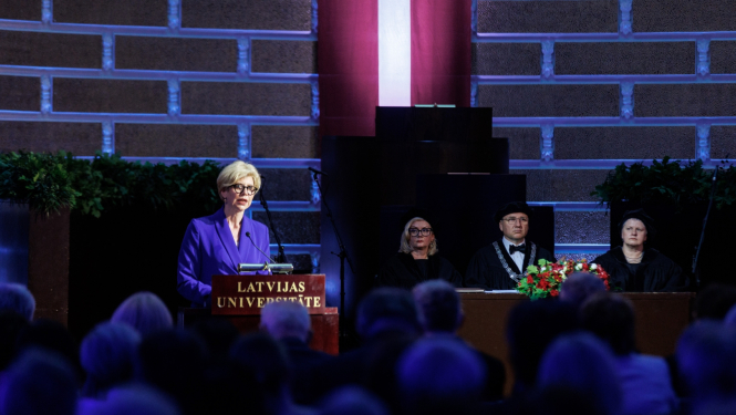 Izglītības un zinātnes ministre Anda Čakša saka uzrunu LU Lielajā aulā, fonā Latvijas karogs