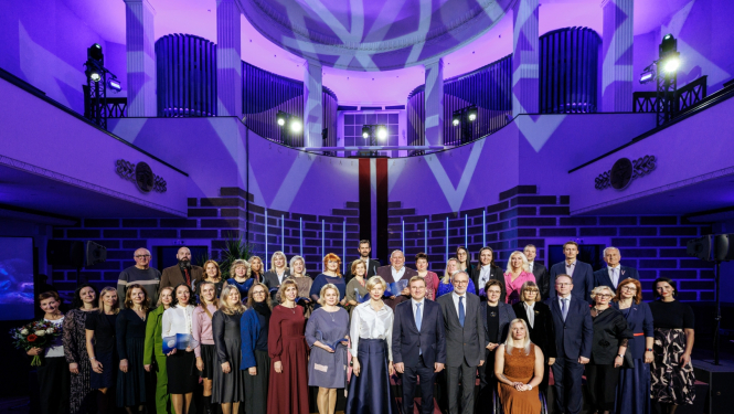 Violetās gaismās izgaismotā LU Lielajā aulā kopõgi stāv visi "Latvijas Gada skolotājs" balvas laureāti, izglītības un zinātnes ministre un LU rektors