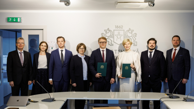 RTU pārstāvju un ministrijas pārstāvju kopbilde pie sienas, uz kuras redzams liels RTU logo