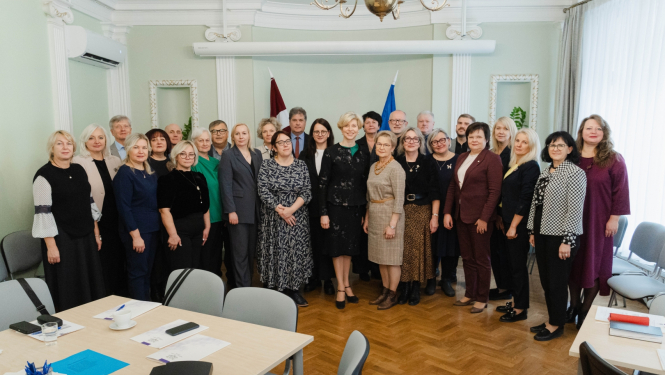 Ministres un skolu direktoru kopbilde pie Latvijas un ES karogiem.