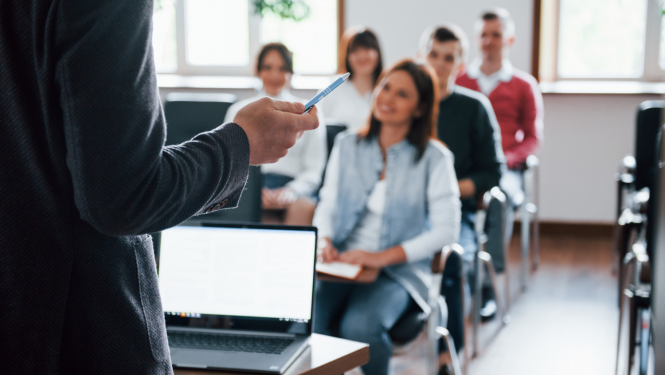 Pasniedzējs stāv ar muguru, studenti sēž klasē