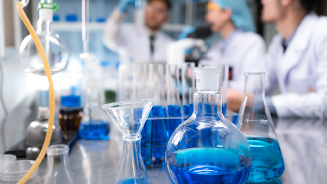 Laboratorija, priekšplānā kolbas ar zilu šķirdrumu