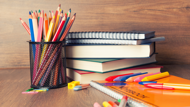 Uz galda stāv grāmatas un zīmuļi melnā glāzē