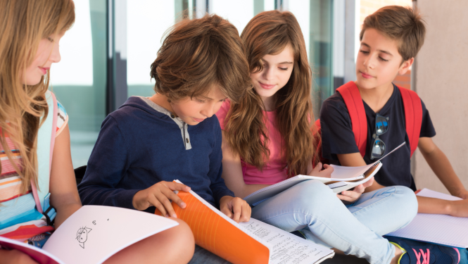 Četri bērni sēž un skatās burtnīcās