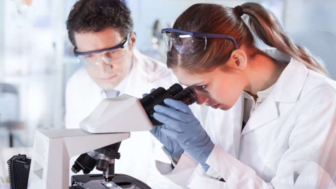 Pētnieks un pēniece sēž laboratorijā, sieviete skatās mikroskopā