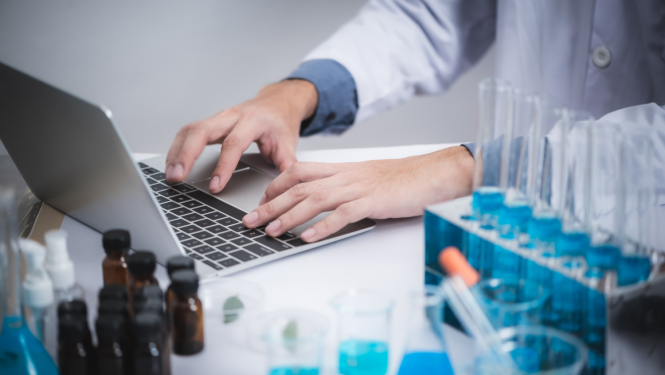 laborants strādā pie datora. Blakus stāv ķīmijas aprīkojums