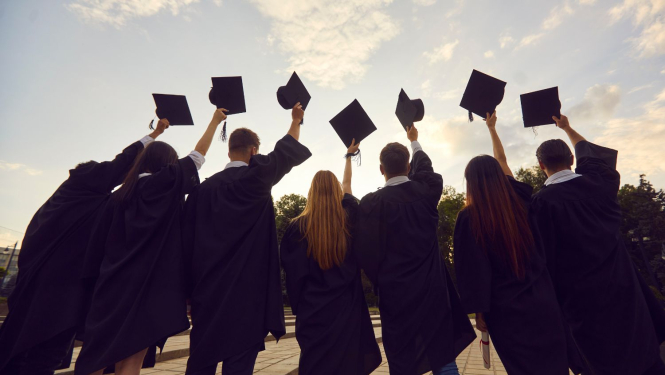Augstskolas absolventi mantijās ar paceltām cepurēm