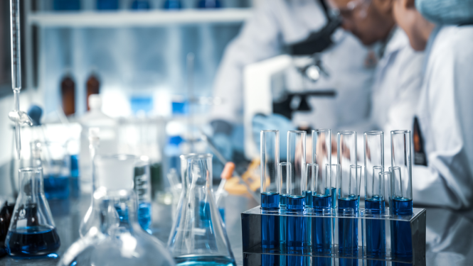 Zinātnieki strādā laboratorijā, priekšplānā mēģenes ar zilu šķidrumu 