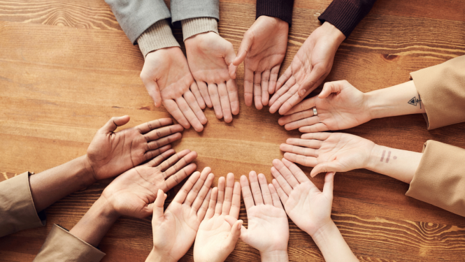 Vairāku jauniešu rokas ar uz galda ar plaukstām uz augšunovietotas aplī