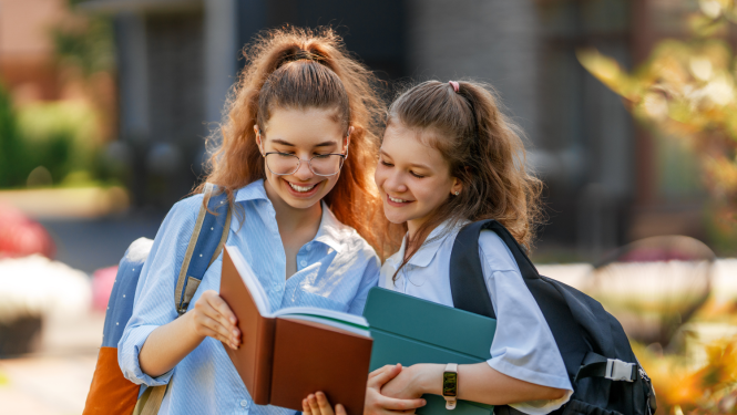 Divas meitenes priecīgas stāv ārā un skatās grāmatā