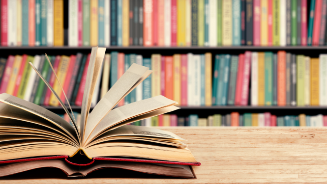 Fonā redzami grāmatu plaukti, priekšplānā divas atvērtas grāmatas