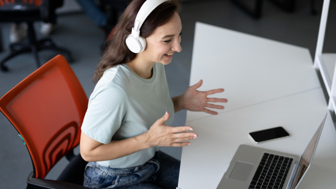 Meitene sēž pie galda, uz kura ir portatīvais dators, un priecīga sarunājas 