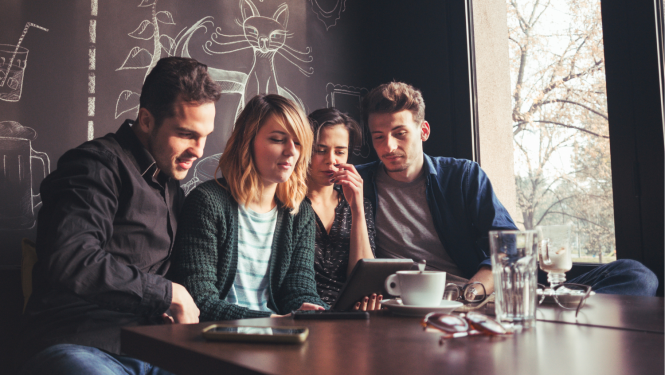 Četri jaunieši sēž kafejnīcā un sarunājas videozvanā caur planšetdatoru