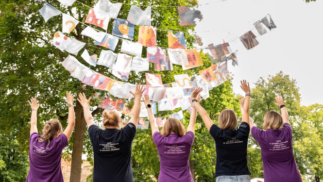 Piecas meitenes redzamas no mugupuses, viņas ir pacēlušas rokas uz augšu, augšā kokos iekārtas virtenes