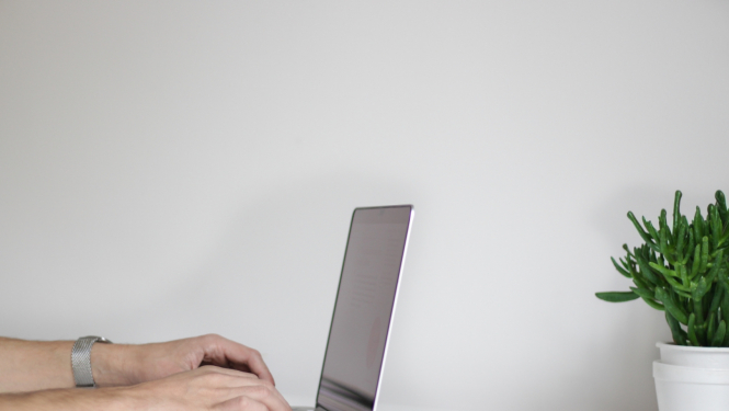 dators uz galda un cilvēka rokas uz klaviatūras