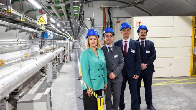 Premjerministre Evika Siliņa un citi Latvijas delegācijas pārstāvji zilās ķiverēs stāv CERN telpās.