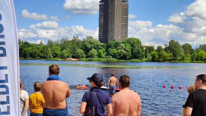 Cilvēki stāv pie Daugavas, viens cilvēks ir glābšanas vestē ūdenī
