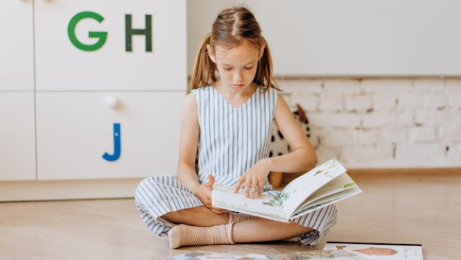 meitene sēž uz zemes un lasa grāmatas. Fonā redzami burti G, H, un J. 