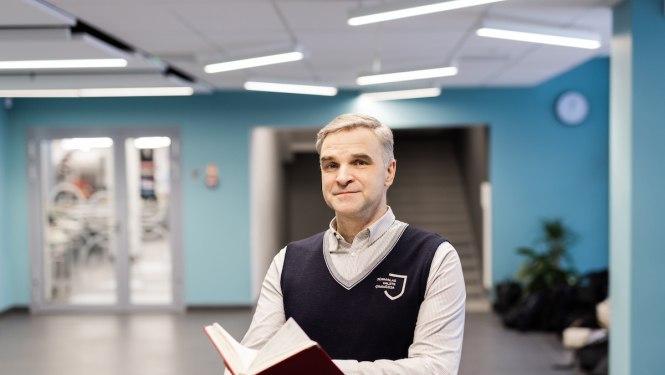 Attēlā redzams skolotājs Jānis no Jūrmalas Valsts ģimnāzijas, kurš rokās tur grāmatu