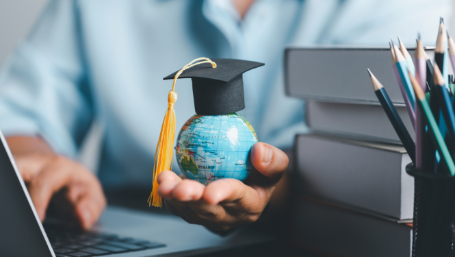 Cilvēka roka tur zemeslodi, uz kuras uzlikta absolventa cepure