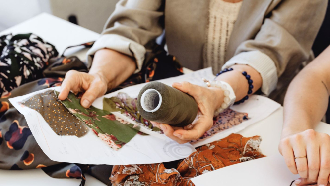 Cilvēki apskata auduma paraugus un diega spolīti, plānojot apģērbu dizainu