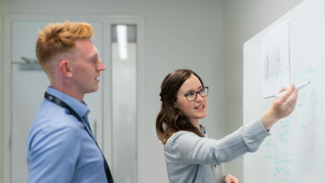 A woman writes on a blackboard, explains information to a man. The image is for illustrative purposes only..