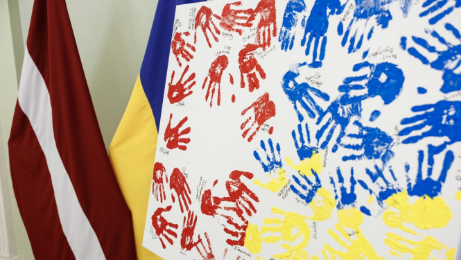 Latvijas un Ukrainas karogi, priekšplānās balts audekls ar krāsā iemērktiem rokas nospiedumiem sarkanā, zilā un dzeltenā krāsā