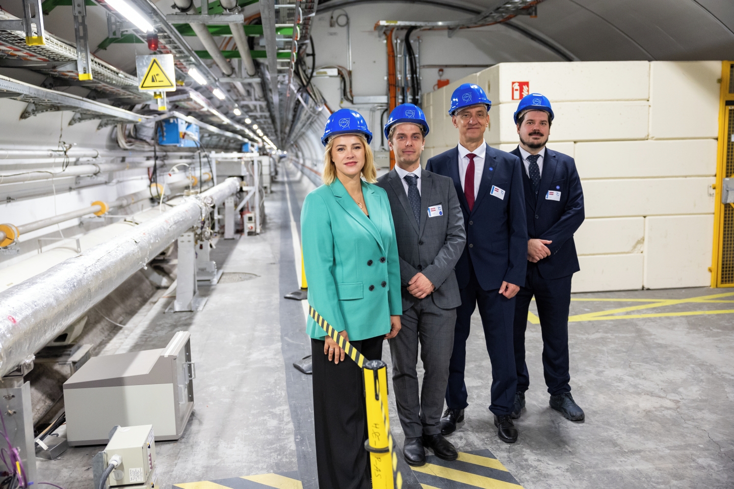 Premjerministre Evika Siliņa un citi Latvijas delegācijas pārstāvji zilās ķiverēs stāv CERN telpās.
