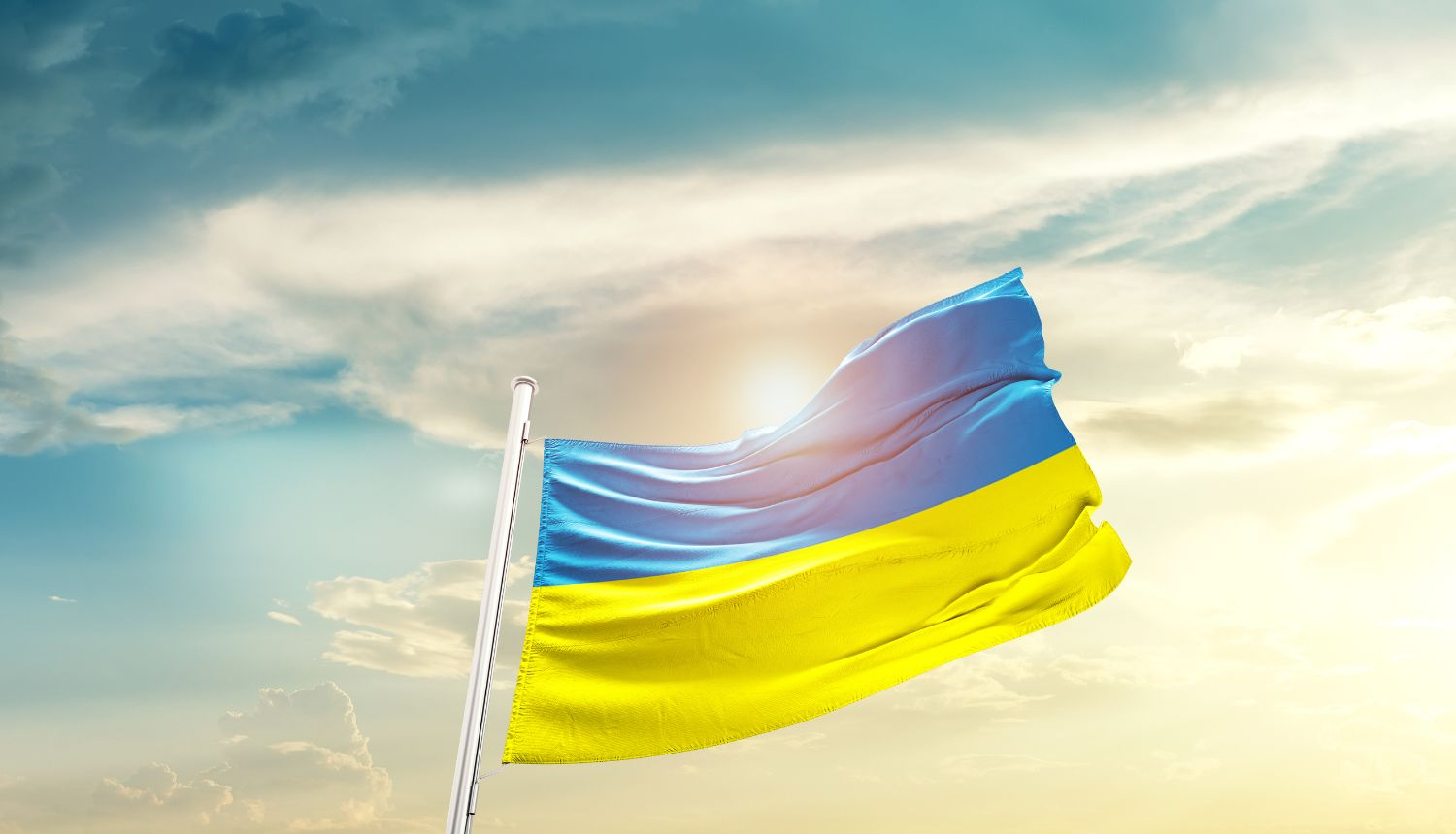 Ukrainas karogs plīvo vējā uz saulrieta fona