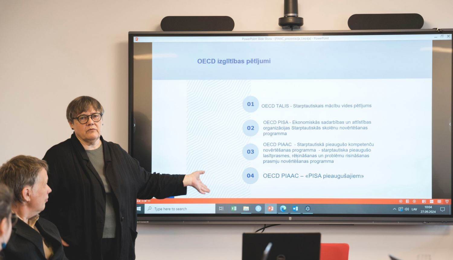 Seminārā Aija Zobena stāsta, fonā liels ekrāns ar prezentāciju