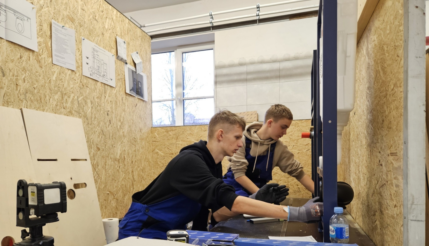 Divi puiši skrūvē instalāciju, apkārt skaidu plākšņu sienas