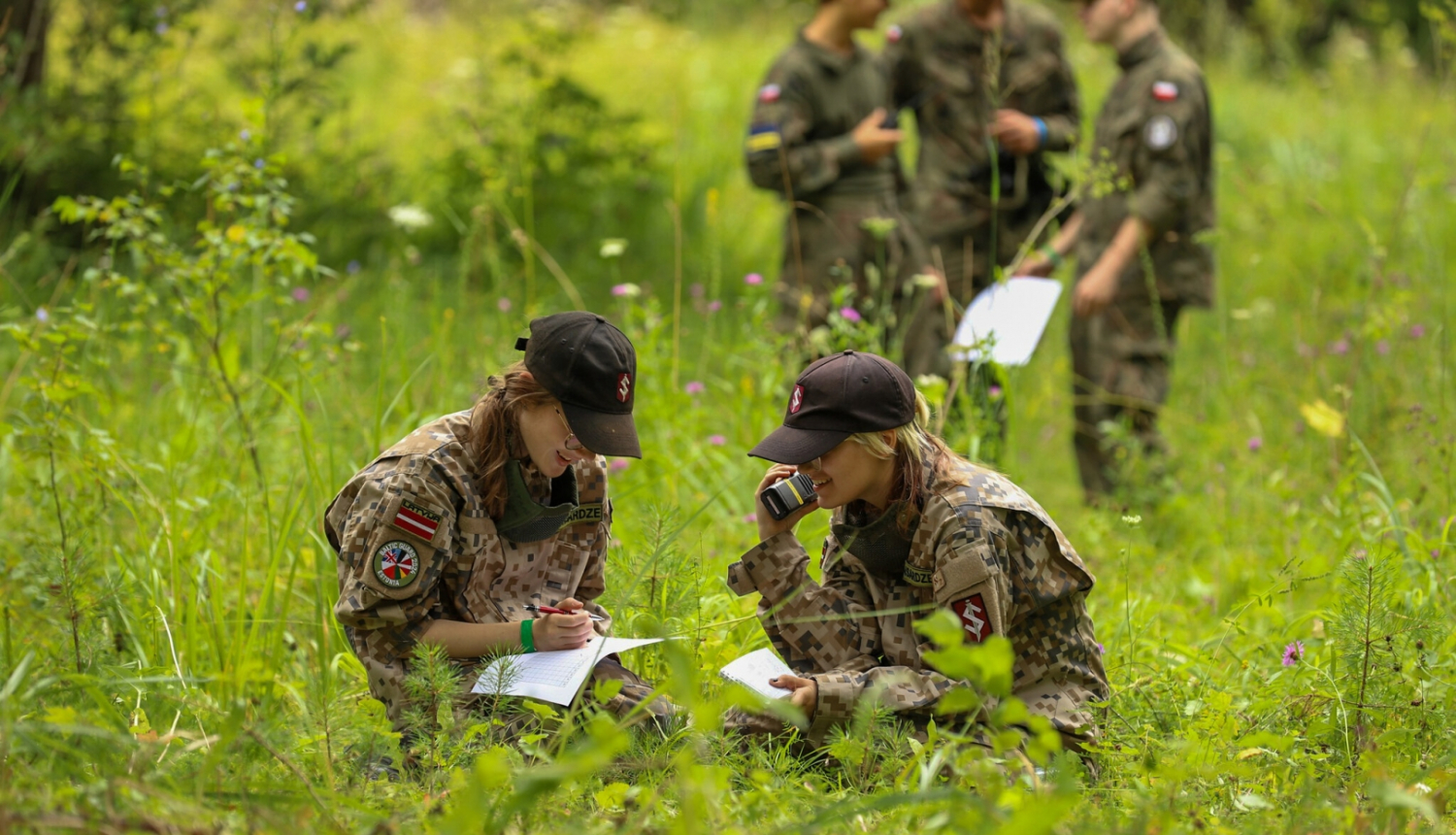 Divas meitenes formastērpos sēž pļavā ar rāciju un karti