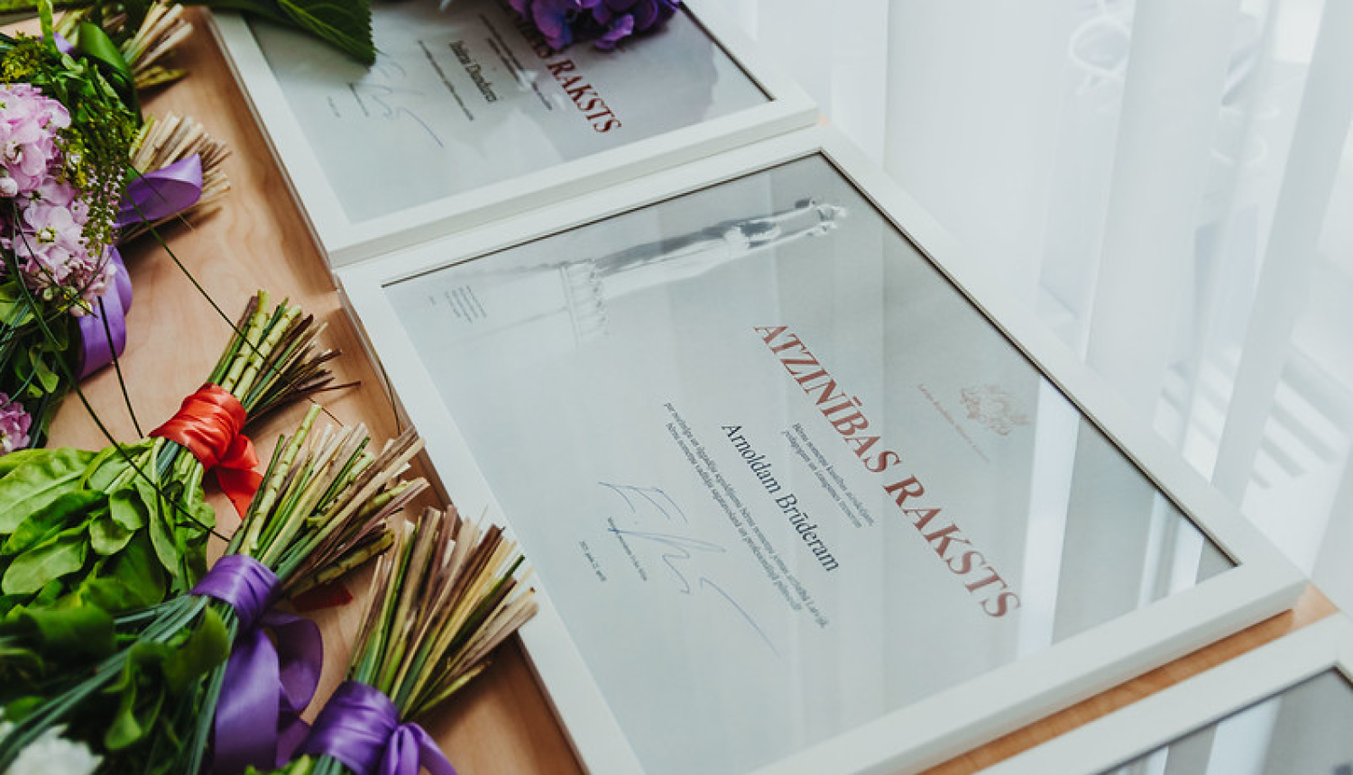 Ministru kabineta Atzinības raksti. Blakus stāv puķu pušķi.