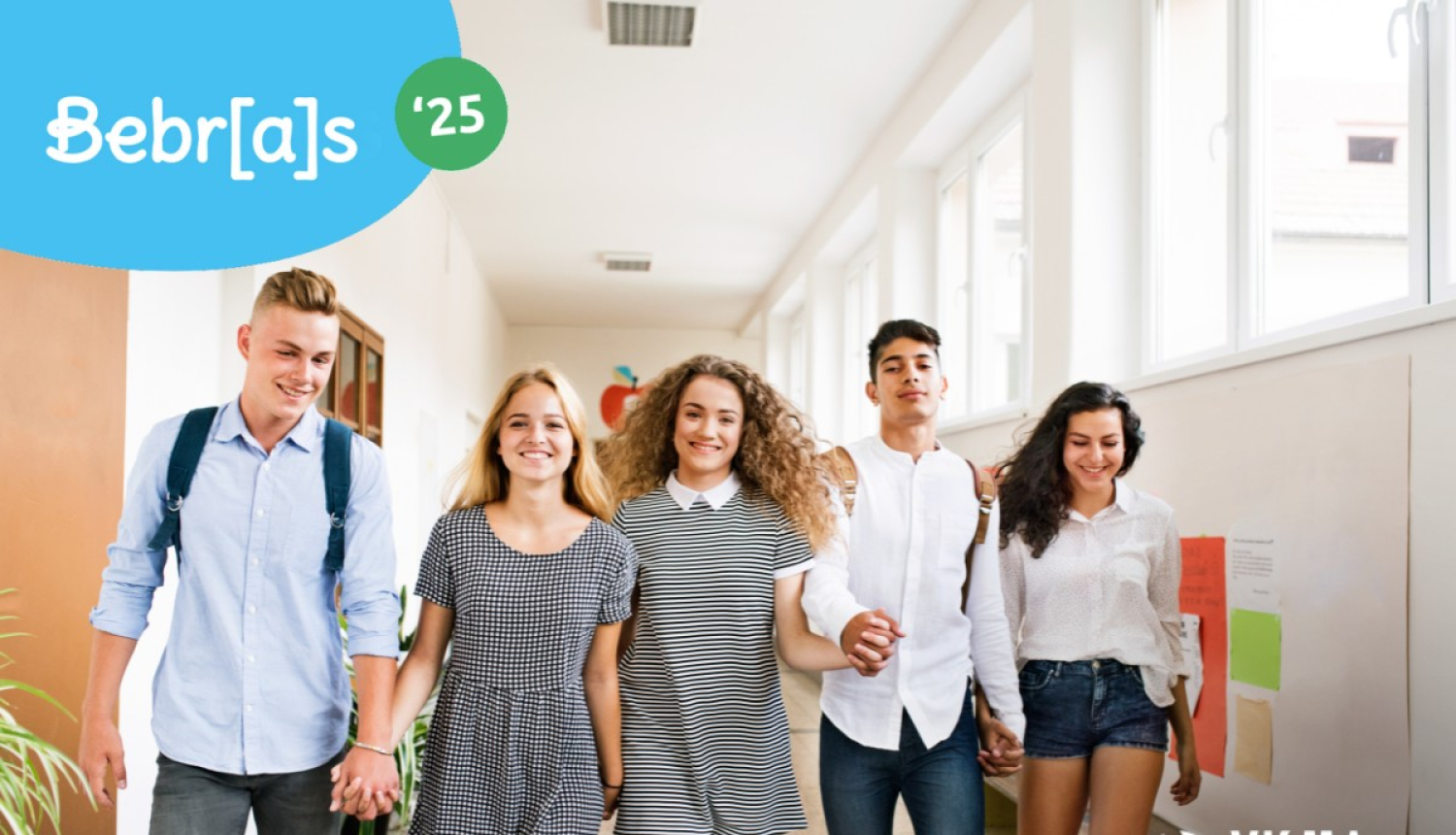 Jaunieši iet pa skolas gaiteni sadevušies rokās. 