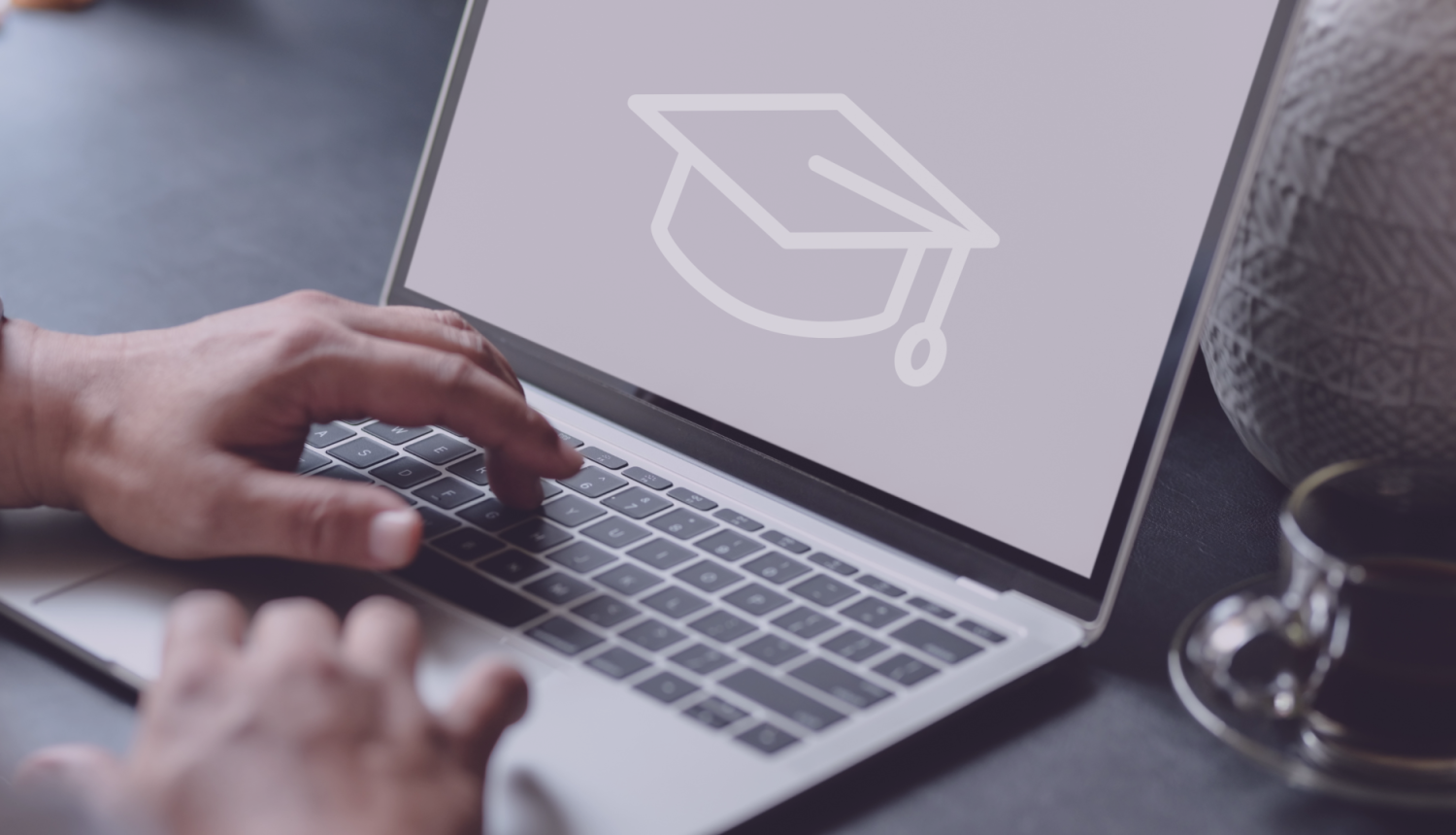 Cilvēks stradā pie datora, datorā redzams absolventu cepure