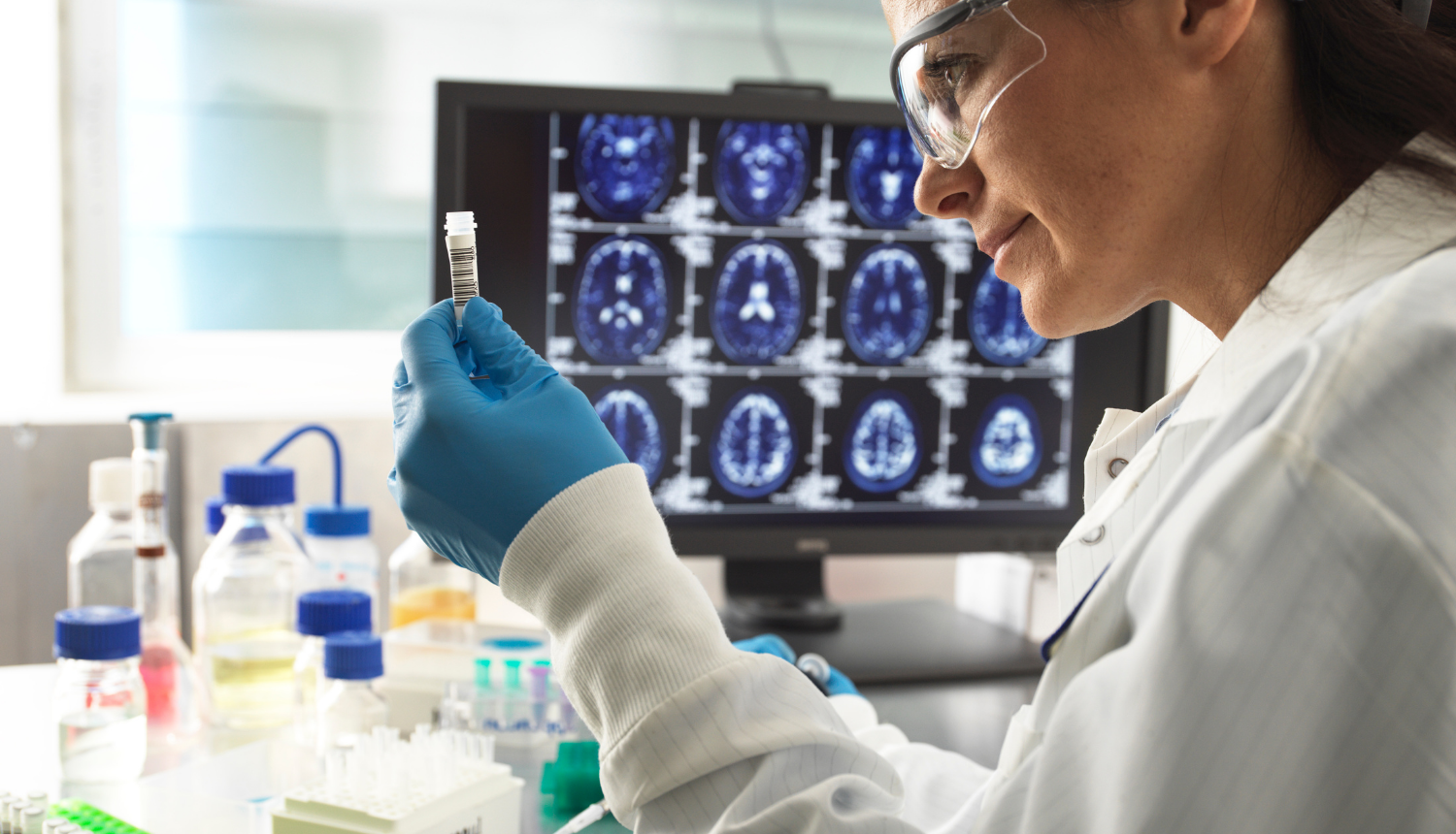 Pētniece skatās uz mēģeni, fonā ekrāns, kurā redzams galvas rentgens