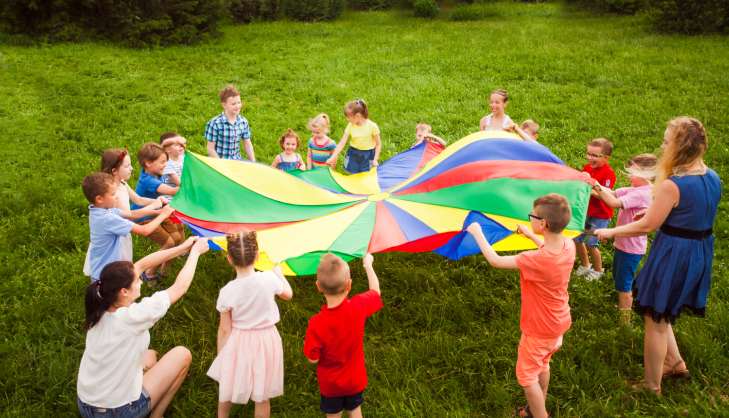 Bērni spēlējas pļavā ar spēļu izpletni