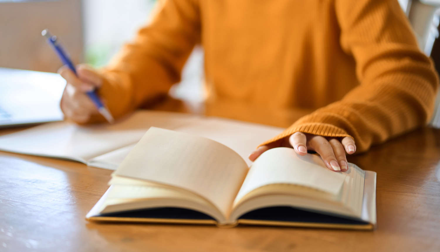 Cilvēks veic pierakstus kladē un pēta grāmatu