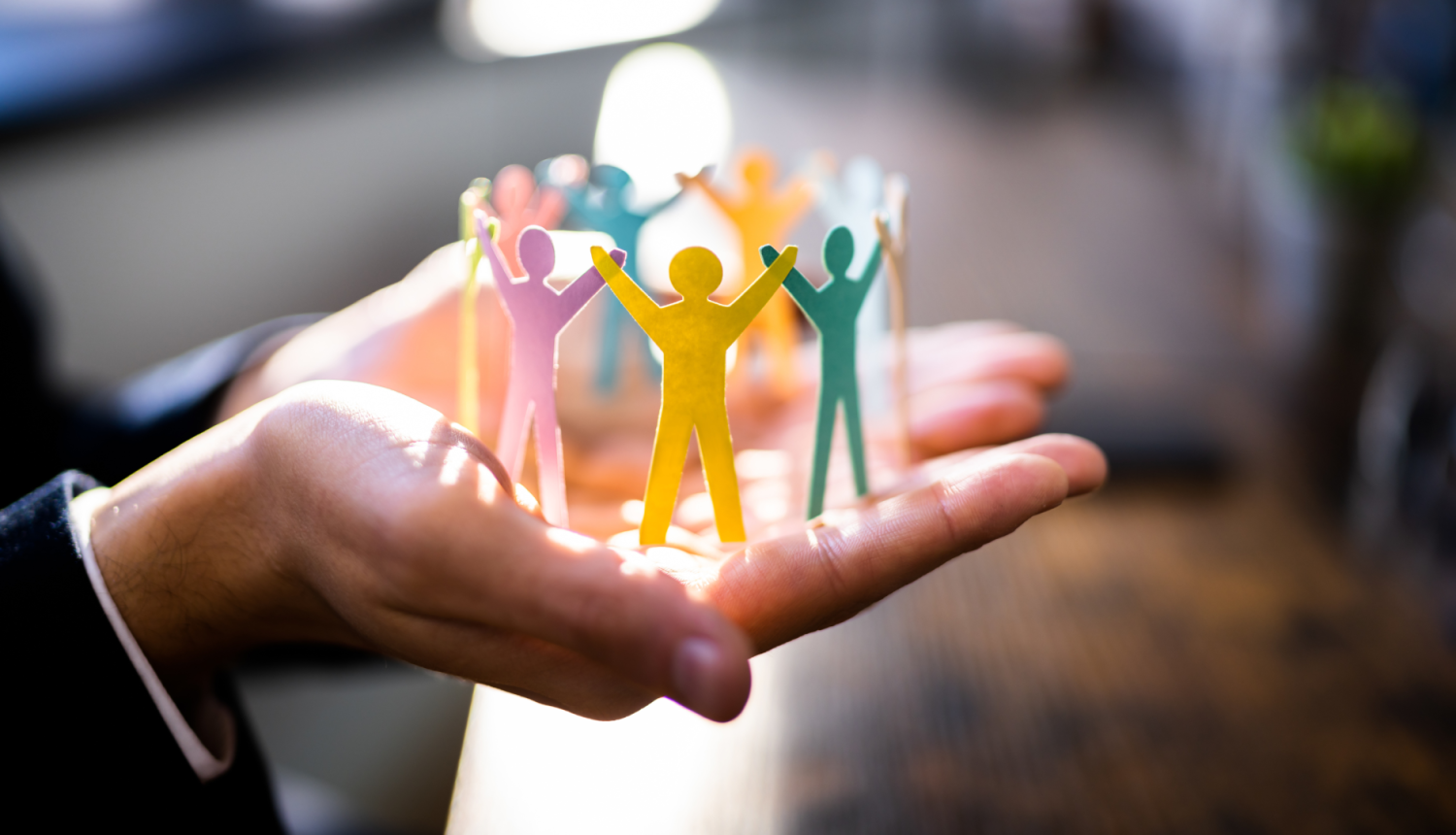 Cilvēks rokās tur papīra cilvēciņus, kuri ir sadevušies rokās.