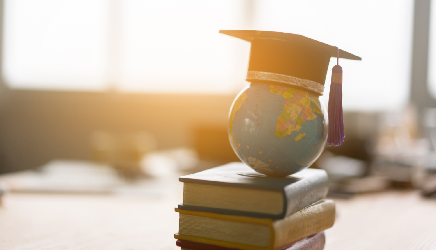 stāv grāmatu kaudzīte, uz tās globuss ar absolventa cepuri